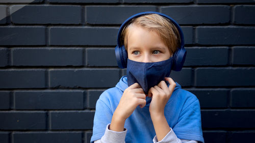 Close-up of boy wearing mask looking away while standing against wall outdoors