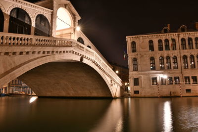 Arch bridge over river in city at night