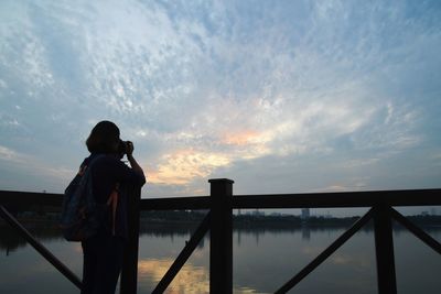 Rear view of man photographing against sky during sunset