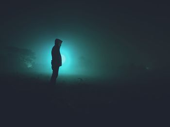 Silhouette man standing on illuminated street light against sky at night