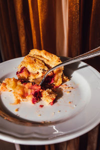 Half eaten slice of rhubarb custard pie on white plate with fork with golden curtain background