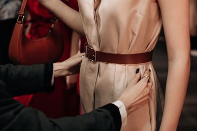 Female hands preparing fashion model dressed in beige long dress with brown belt