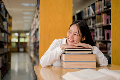Smiling woman leaning on stacked book in library