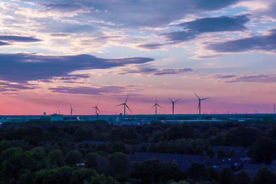 Wind turbines on field against sky during sunset