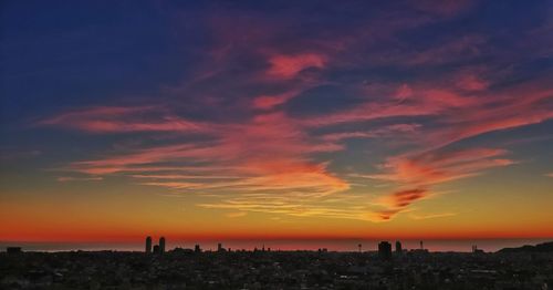 Silhouette of city against cloudy sky at sunset