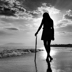 Rear view of silhouette woman standing at beach against sky