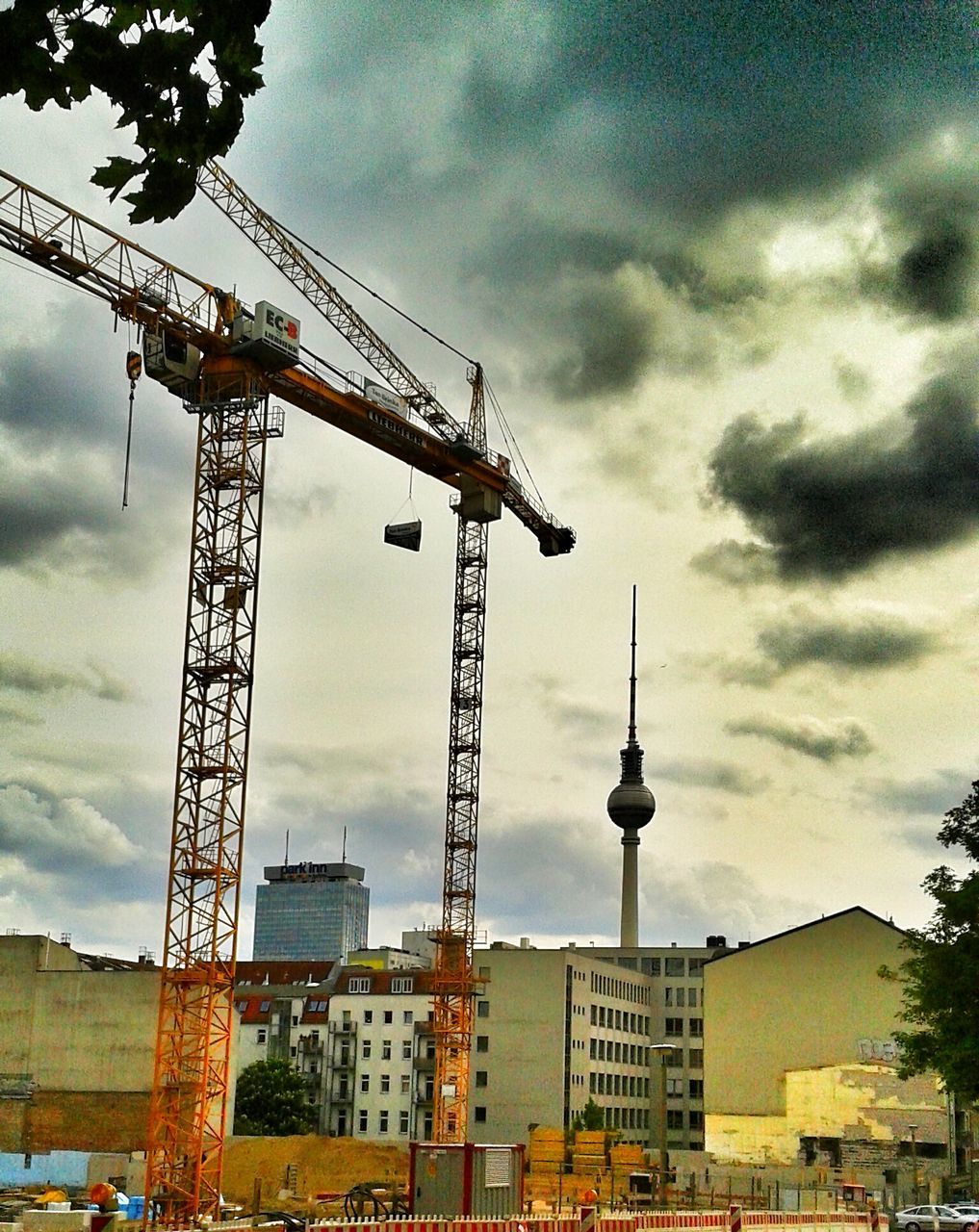 architecture, building exterior, built structure, sky, cloud - sky, cloudy, crane - construction machinery, construction site, low angle view, development, crane, city, cloud, tall - high, industry, tower, communications tower, weather, outdoors, construction