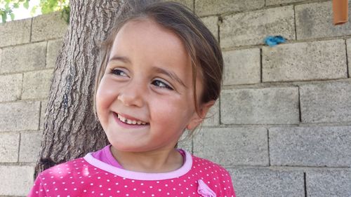 Close-up of smiling girl standing against wall