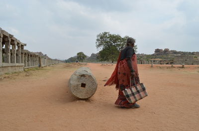 Rear view of woman walking on field against sky