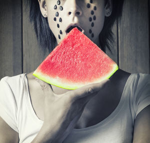 Midsection of mid adult woman eating watermelon against wooden wall