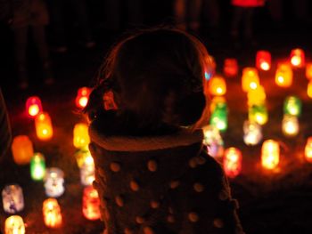 Girl wearing warm clothing while standing by colorful illuminated decorations at night