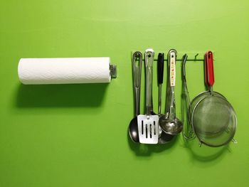 Close-up of tissue roll by kitchen utensils hanging from hooks on green wall