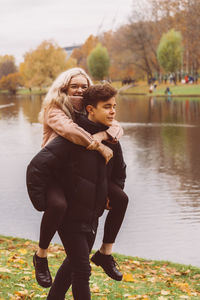 Boyfriend piggybacking girlfriend against lake in park