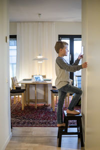 Boy standing on stool while using digital tablet mounted on wall at smart home