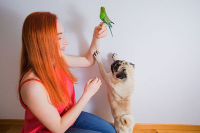 Smiling woman holding bird with dog at home