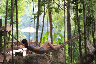 Side view of woman relaxing on hammock in forest