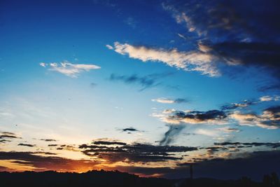 Low angle view of sunlight streaming through clouds during sunset