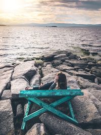 Man sitting at beach against sky during sunset