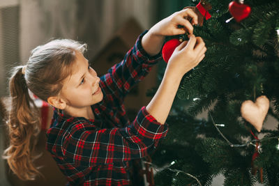 Happy little blonde in new year's home clothes, decorates the christmas tree and smiles. 