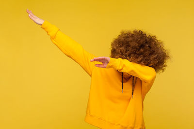 Woman gesturing while standing against yellow background