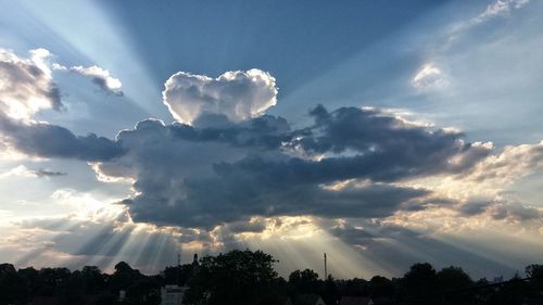 Low angle view of sunlight streaming through clouds