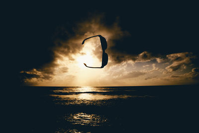 Silhouette sunglasses over sea against cloudy sky during sunset