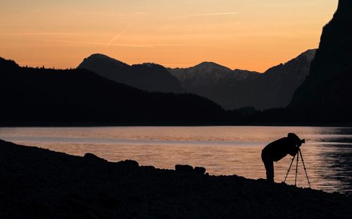 Silhouette man on lake against sky during sunset