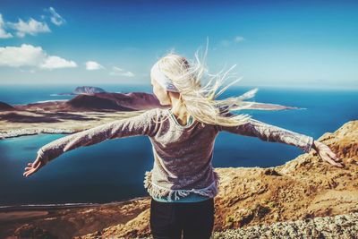 Rear view of woman with arms outstretched by sea against sky