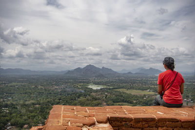 Rear view of man sitting on mountain against sky