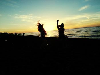 Silhouette people on beach against sky during sunset