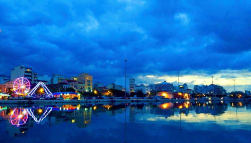 Illuminated city by river against sky at night