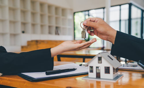 Cropped hands of businessman giving key to colleague in office