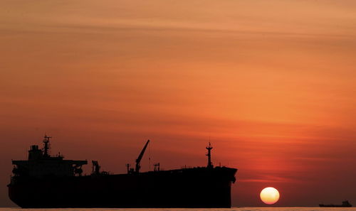 Silhouette ship in sea against orange sky