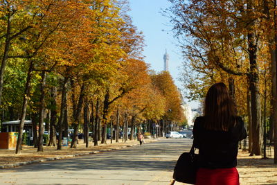 Rear view of woman walking street amidst autumn trees