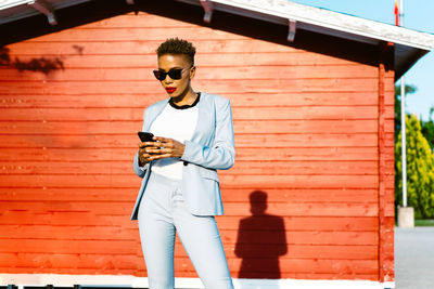 Cheerful african american female in trendy suit using cellphone in sunny town
