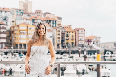 Portrait of smiling young woman standing against buildings in city