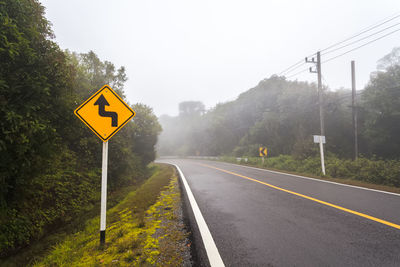 Windy forest road with a curve sign on a foggy day at doi inthanon national park, thailand