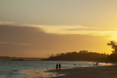 Silhouette people on beach against sky during sunset