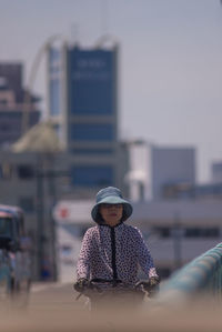 Portrait of woman wearing hat against sky in city