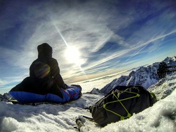 Hiker sitting on snow covered mountain against sky during sunny day