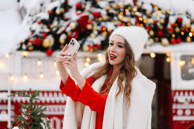 A beautiful young woman with red lips in a warm hat stands by decorated christmas van on the street