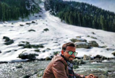 Young man wearing sunglasses while sitting by river during winter