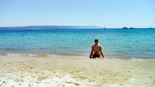 Rear view of shirtless man on beach against clear sky