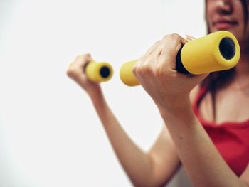 Midsection of woman lifting dumbbells against white background