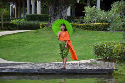 Full length portrait of woman standing on grassland against trees