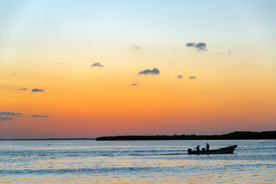 Silhouette men in boat on sea against sky during sunset