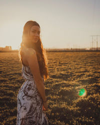 Beautiful woman standing on field against sky during sunset