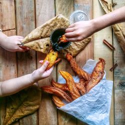 Cropped hands of children eating snacks on wooden table