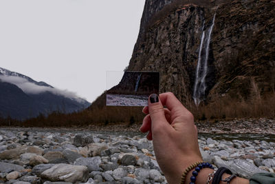 Cropped hand of woman holding photograph against mountain