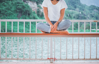 Low section of woman sitting on bench against railing